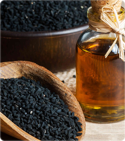 Black seeds in a wooden scoop with a bottle of oil on a wooden surface