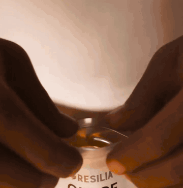 A Resilia pouch opening to reveal golden softgels, one held between two fingers
