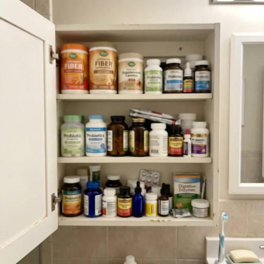 A bathroom shelf crowded with fiber tubs, probiotic bottles, and gut-cleanse teas
