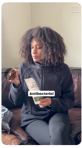 A real customer on her couch holding her Resilia softgel and pouch