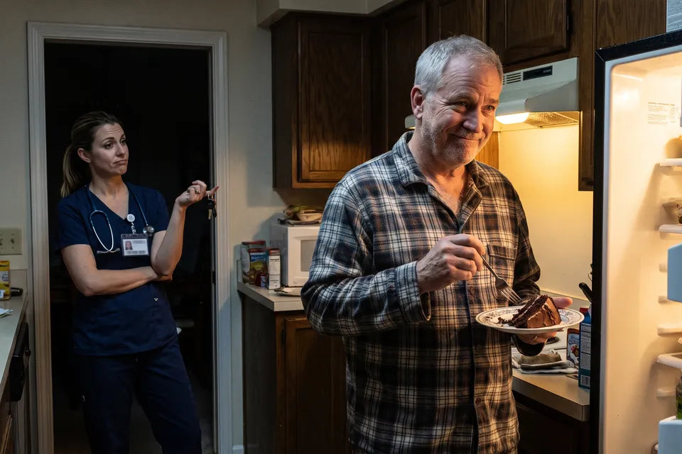 Gary in his pajamas caught eating chocolate cake at the open fridge late at night while his daughter, a doctor in scrubs, watches from the doorway