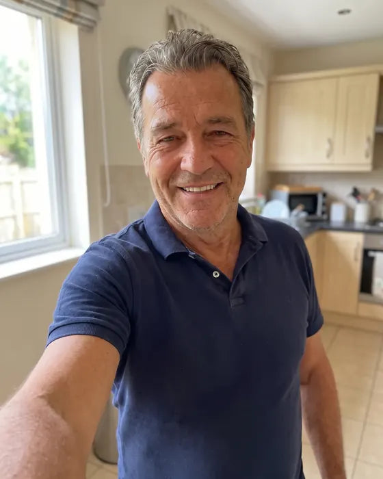 Ray taking a selfie in the same kitchen on day 28, same navy polo fitting neatly, face less puffy, big smile