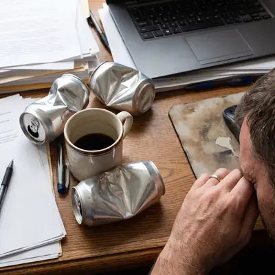 Crushed energy drink cans and a cold coffee on an office desk