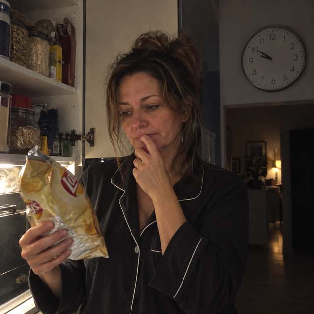 Woman standing at the pantry at night looking at a bag of chips