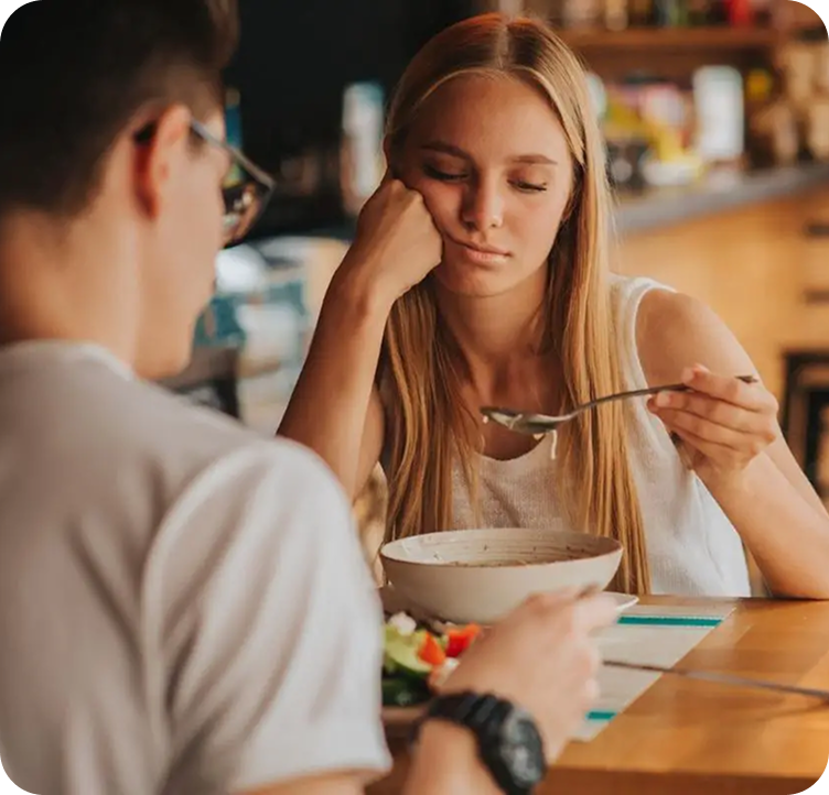 Two people sitting at a table with a bowl of salad and a fork.