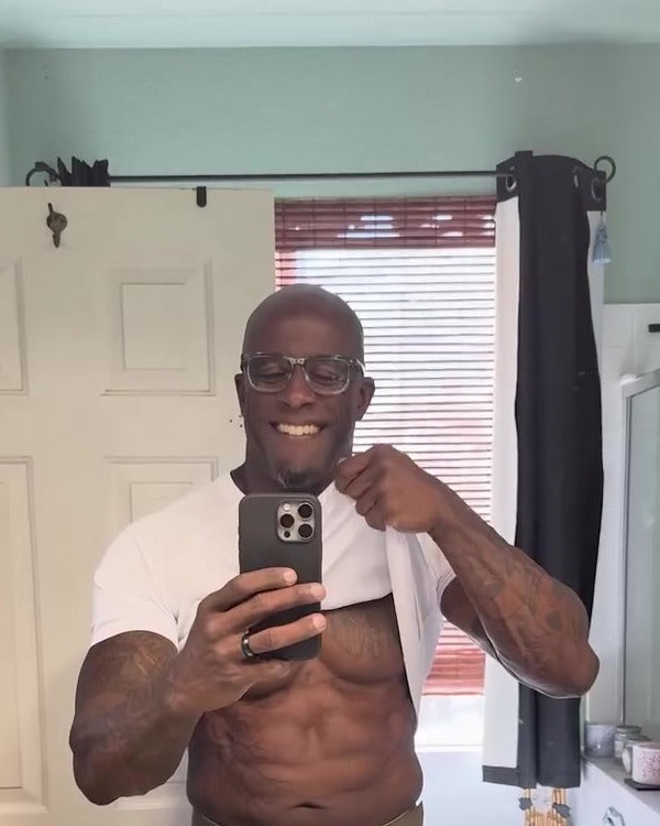 After: a smiling man lifts his shirt in the bathroom mirror to show a lean, toned stomach